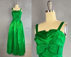 ~1950s long emerald green satin gown with bow and bustle ~Bodice comprised of a straight inner layerwith a split ruched top layer  ~Folded matte satin (cleverly using the reverse of the satin) at waistline creates belted appearance with   matte emerald bow  ~Bow with snap closure at back on waistline from which falls a beautiful bustle ~Gathering at hips and large pleats down center of skirt  ~Lined with tulle that fills out and structures the skirt  ~Metal back zipper  Size - Small, Extra Small Green Satin Gown With Pleated Bodice, Green Satin Evening Gown, Vintage Fitted Green Gown, Green Silk Formal Gown, Vintage Green Gown For Wedding, 1950s Style Green Formal Dress, Green 1950s Style Formal Dress, Vintage Green Wedding Gown, Green Ballgown