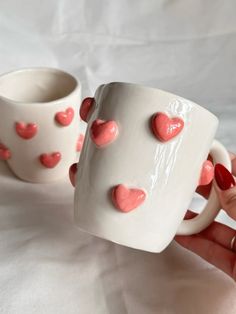 two coffee mugs with hearts on them are being held by someone's hand