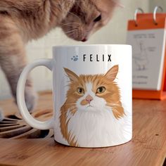 a cat standing on top of a wooden table next to a white coffee mug with a brown and white cat's face