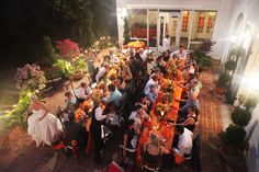 a large group of people sitting at tables in front of a house with lights on