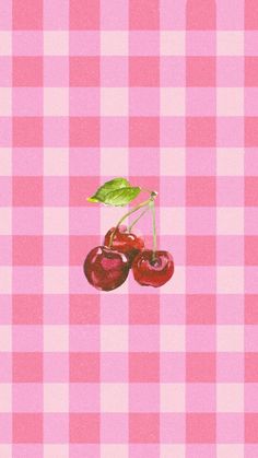 two cherries on a pink and white checkered tablecloth with a green leaf