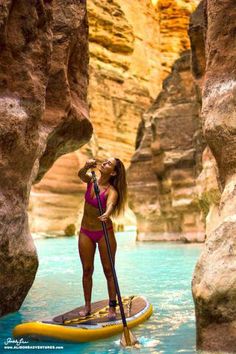 a woman standing on a paddle board in the middle of a river surrounded by rocks