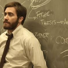 a man standing in front of a blackboard with writing on it and wearing a tie