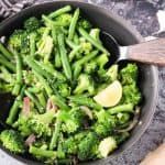 broccoli is being cooked in a skillet with a wooden spoon on the side