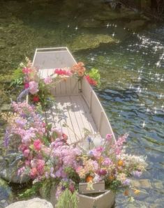 a row boat filled with lots of flowers on top of a body of water next to rocks