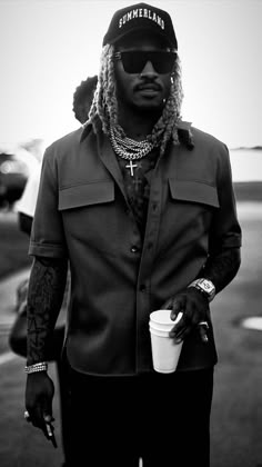 a man with dreadlocks holding a drink and looking at the camera while standing in an airport parking lot