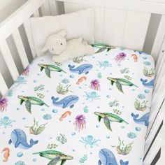 a white crib with a blue and green sea animals print on it, next to a stuffed animal