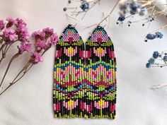 a pair of beaded earrings sitting on top of a table next to purple flowers