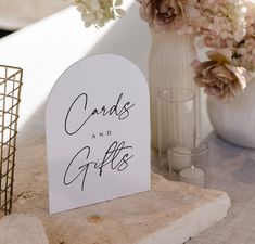 a card and gifts sign sitting on top of a table next to vases with flowers