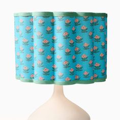 a blue lamp shade with pink flowers and green trim on a white base, in front of a white background