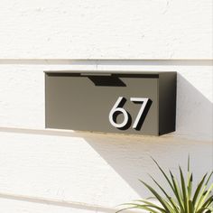 a black mailbox mounted to the side of a white building with a plant next to it