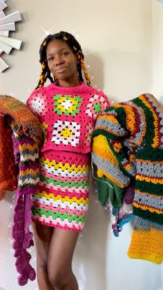 a woman in a colorful crochet dress standing next to some sweaters