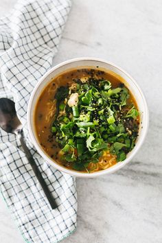 a bowl of soup with broccoli and other vegetables on the side next to a spoon