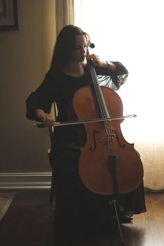 a woman playing the cello in front of a window