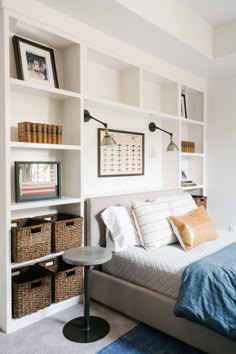 a bed sitting in a bedroom next to a shelf filled with books and baskets on top of it