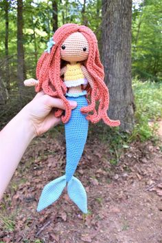 a hand holding a crocheted doll in the woods