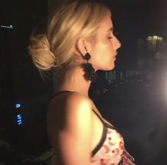 a woman standing in the dark with her hair pulled back and wearing large black earrings