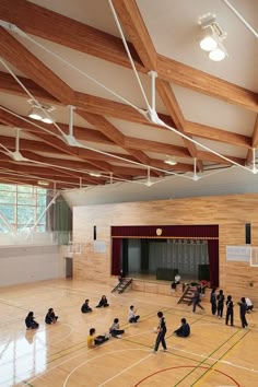 an indoor basketball court with people sitting on the floor and standing in front of it