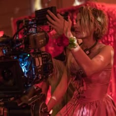 a woman in a pink dress standing next to a camera and holding her arm out