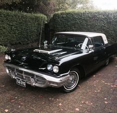 an old black and white car parked in front of a hedge