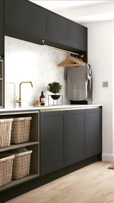 a kitchen with black cabinets and white counter tops, baskets on the sink and hanging clothes