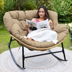 a woman reading a book while sitting in a swing chair on top of a rug