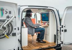 a man sitting at a desk in the back of a van with its door open