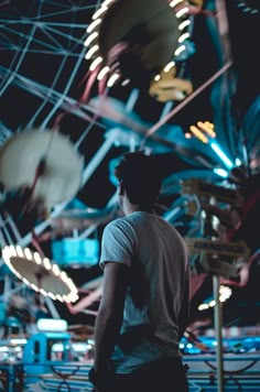 a man standing in front of a ferris wheel at an amusement park with lights on