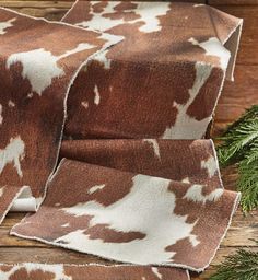 the cow print fabric is brown and white with black spots on it, as well as pine needles