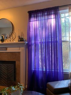 a living room filled with furniture and a fire place next to a window covered in purple sheer curtains