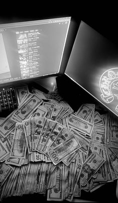 a pile of money sitting next to a laptop computer on top of a bed of dollar bills