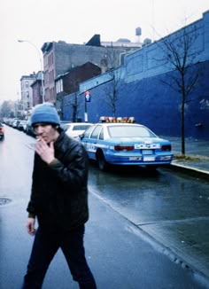 a man is walking down the street on a rainy day with his hand in his mouth