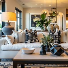 a living room filled with white couches and pillows on top of a rug next to a coffee table