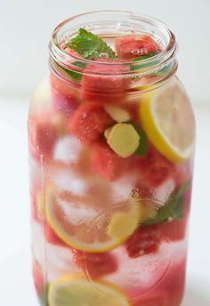 a mason jar filled with watermelon, lemon and mintade slices on a white surface