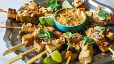 chicken skewers with dipping sauce and lime wedges on a plate, ready to be eaten