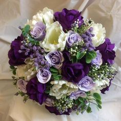 a bridal bouquet with purple and white flowers on a white sheeted cloth background