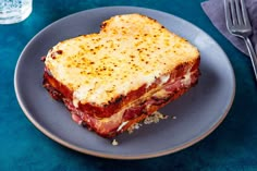 a piece of toasted meat and cheese sandwich on a plate next to a fork