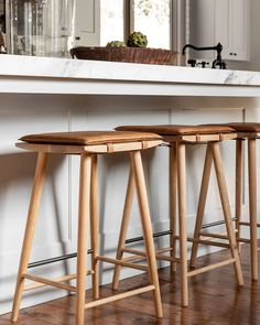 three wooden stools sitting on top of a hard wood floor next to a counter