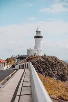 a white lighthouse on top of a hill next to the ocean with people walking by