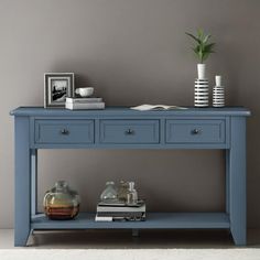 a blue console table with two drawers and a vase on the top, in front of a gray wall