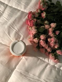 a white cup sitting on top of a bed covered in pink flowers next to a bouquet of roses