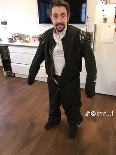 a man dressed in black and white standing on a hard wood floor next to a kitchen