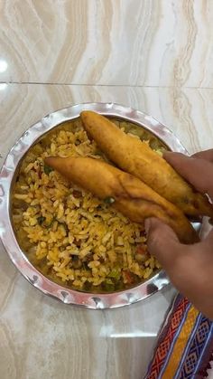 a person is holding two pieces of food in front of a plate with rice and fish sticks