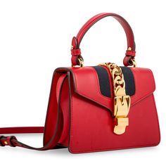 The Gucci Sylvie is one of those bags that became a classic the moment it landed in stores. The red hue is complimented by a white, blue and red woven fabric strap, ideal for cross-body usage - and if one strap wasn't enough, don't worry, you can find an additional red leather shoulder strap inside. This stunning bag is an absolute necessity, especially during holiday season. With a gold buckle chain prominently depicted on the front flap, the Sylvie is luxurious, glamorous and the perfect compliment to any neutral-toned or monochromatic outfit. Whether you dress the Sylvie up or down, you can be sure this bright, bold piece is the ideal accessory for any occasion. Sleek, stylish, sophisticated, but youthful and playful at the same time, the Sylvie is a well-worthy addition to any luxury h Mini Top Handle Bag, Gucci Sylvie, Monochromatic Outfit, Mini Top, Fabric Strap, Dior Shoes, Red Fabric, Exclusive Bag, Handle Bag