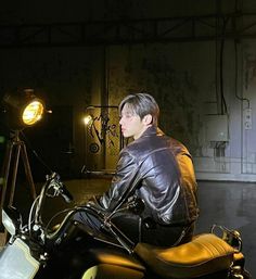 a man sitting on top of a motorcycle in a dark room with a light on