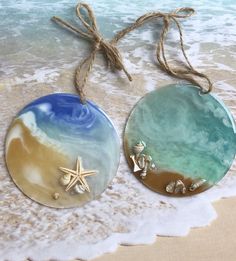 two round glass ornaments with starfish and shells on the beach next to the ocean