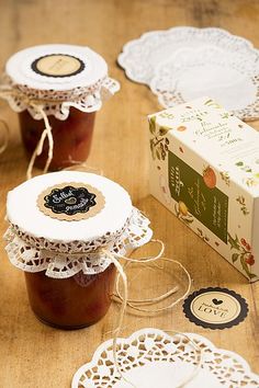 three jars filled with jam sitting on top of a wooden table next to paper doidles