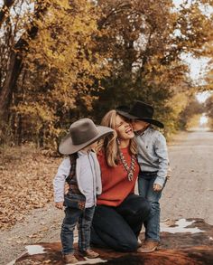 a mother and her two children are sitting on a log in the middle of an empty road