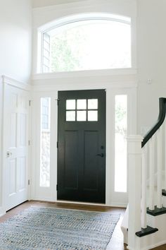 a black door is in the middle of a white room with an area rug on the floor