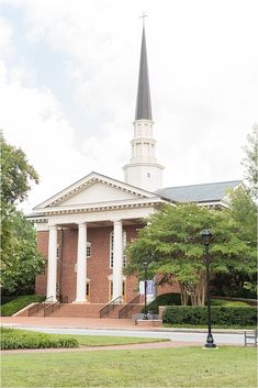 an old brick church with a steeple and white columns on the front, surrounded by greenery